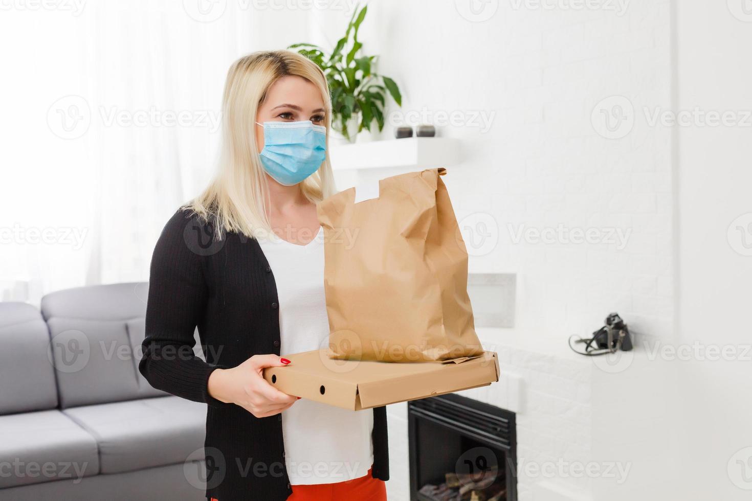 ung kvinna bär medicinsk mask tar emot paket från leverans man inomhus. förebyggande av virus spridning foto