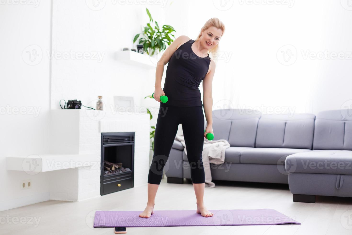 en tunn europeisk flicka håller på med stretching övningar på Hem på en yoga matta, strålar av ljus glans från de fönster. blossa. karantän sport. foto