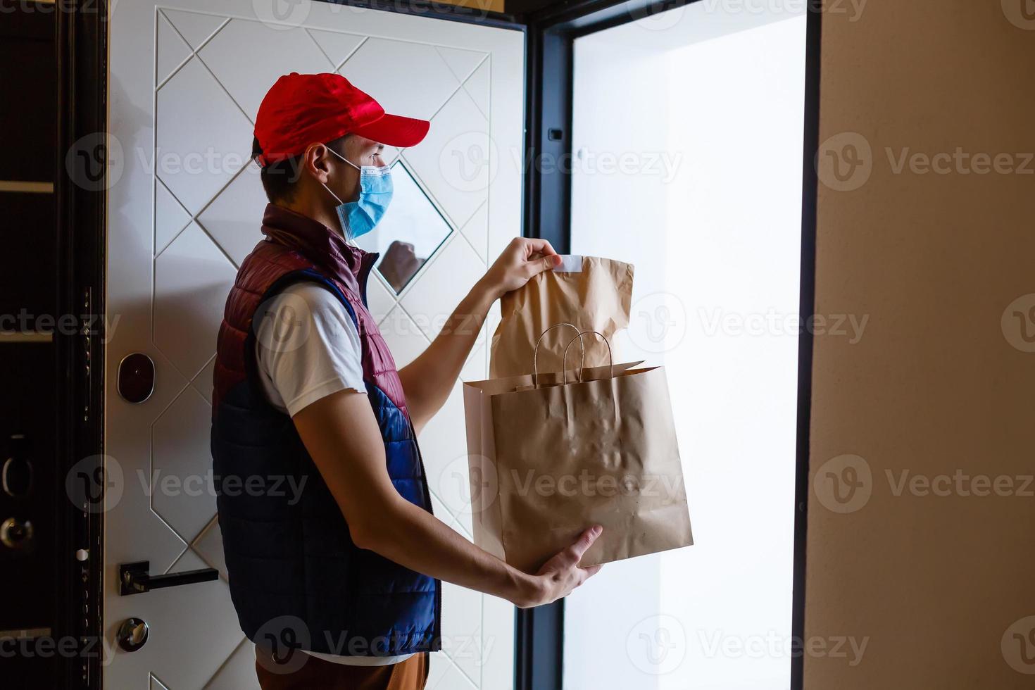 leverans man innehav papper väska med mat på vit bakgrund, mat leverans man i skyddande mask foto