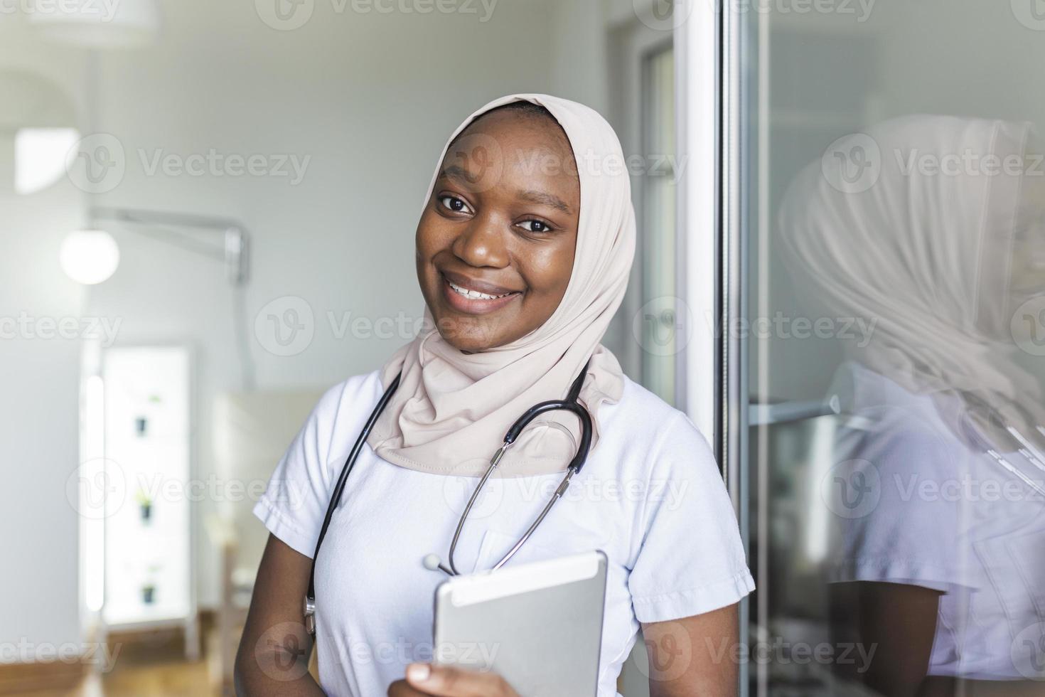 ung kvinna muslim afrikansk klinikern läkare i scrubs använder sig av pekplatta medan kommunicerar med patienter uppkopplad foto