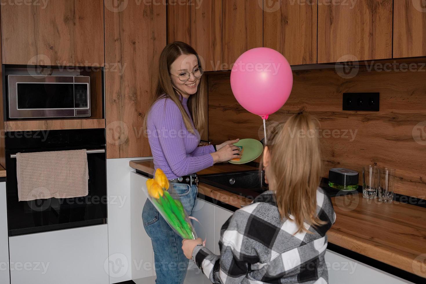 de dotter gratulerar henne mor på mors dag, ger henne en ballong och blommor. de kvinna tvättar de maträtter och är upptagen på detta tid med hushåll sysslor. foto