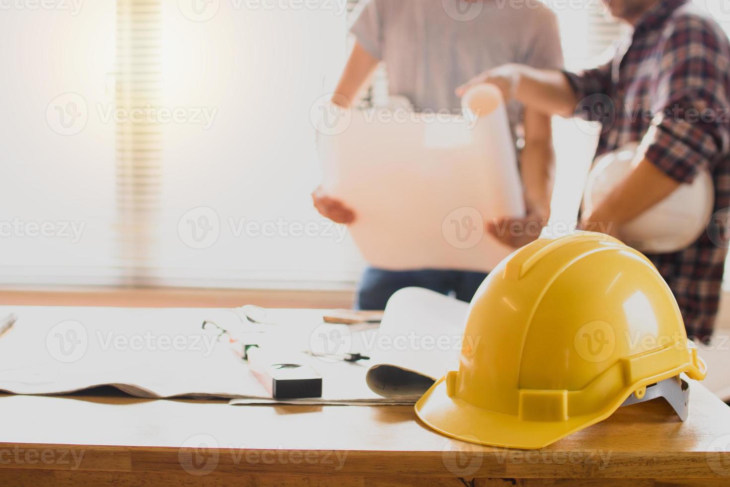 konstruktionsskyddshjälmar på bordet med ingenjör som håller ritningsbakgrund foto