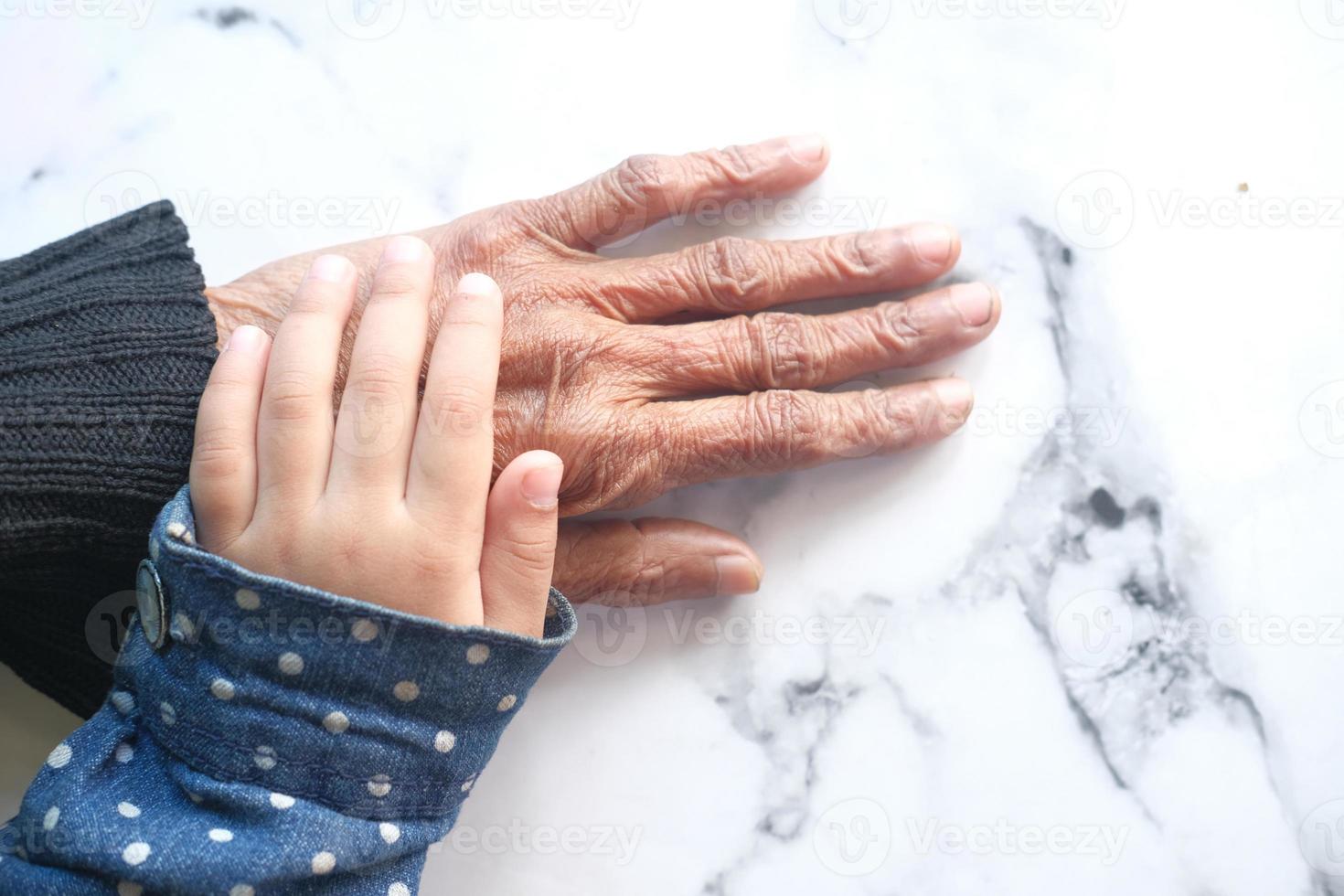 detalj skott av barn flicka håller handen av en äldre kvinnor foto