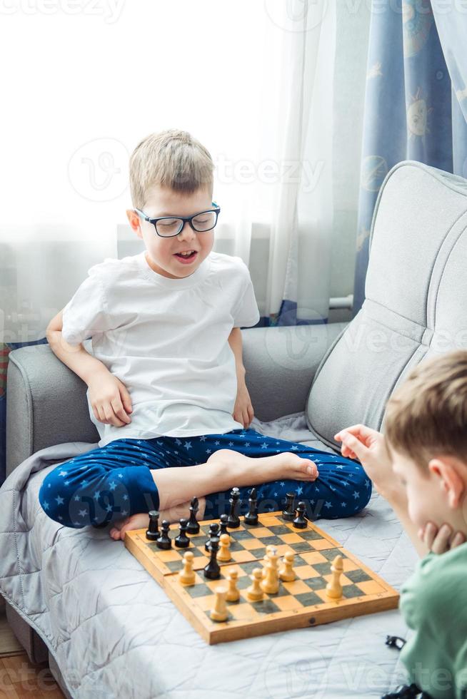 Pojkar spelar trä- schack liggande på en grå soffa i främre av de fönster foto