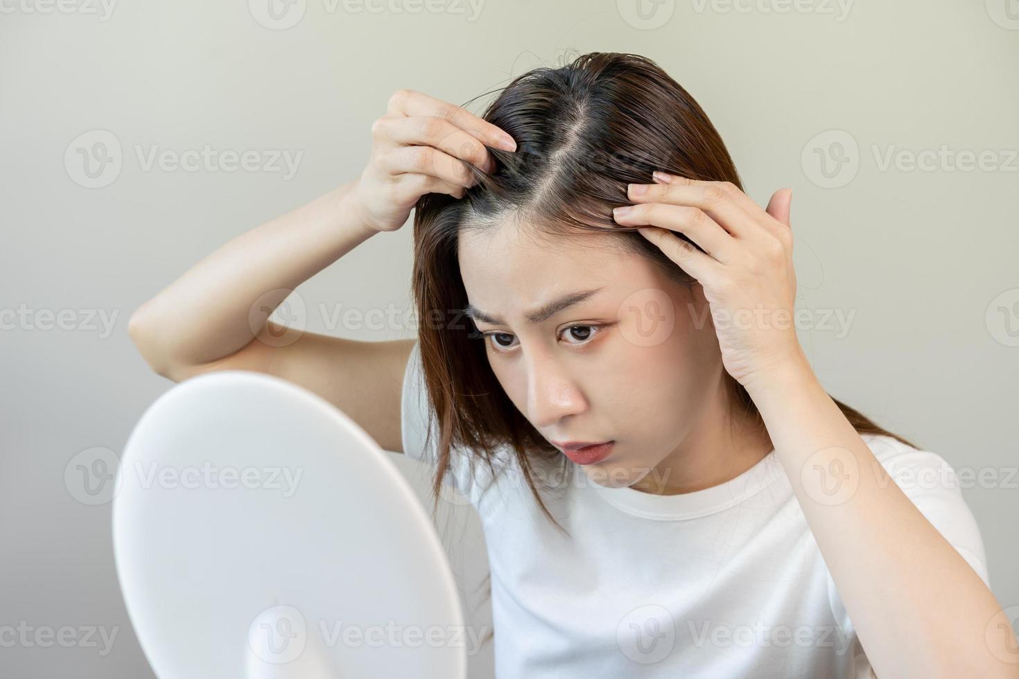 skadad hår, ansikte allvarlig asiatisk ung kvinna oroa ser på skalp i spegel, hand i ha sönder in i främre hår förlust, tunn problem symptom på Hem. hälsa vård schampo skönhet, isolerat på bakgrund. foto