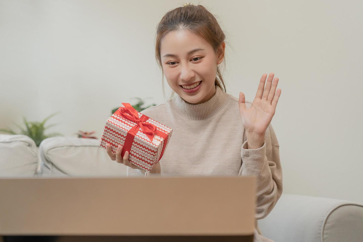 fira på jul afton, ny år dag säsong, Söt asiatisk ung kvinna, flicka använder sig av bärbar dator dator, hälsning på video ring upp under social distans, innehav gåva låda, Lycklig till skaffa sig närvarande, glad xmas foto