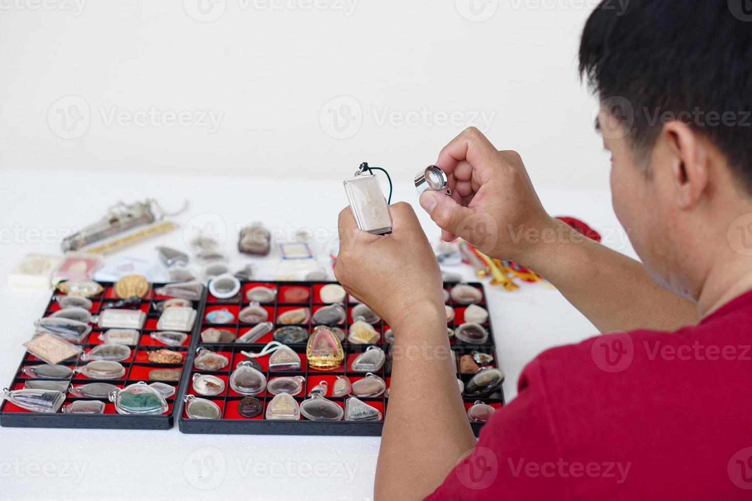 närbild händer håll buddha amulett och förstorande glas till kolla upp detaljer och figur av objekt. begrepp, tro och tro i helig och tur för buddhister. insamling amulett som hobbyer, utbyta eller handel. foto