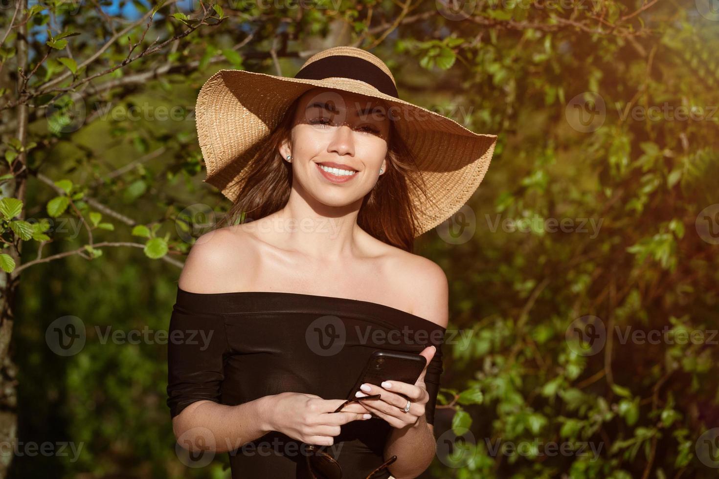 skön Lycklig kvinna i hatt med telefon i hand i sommar foto