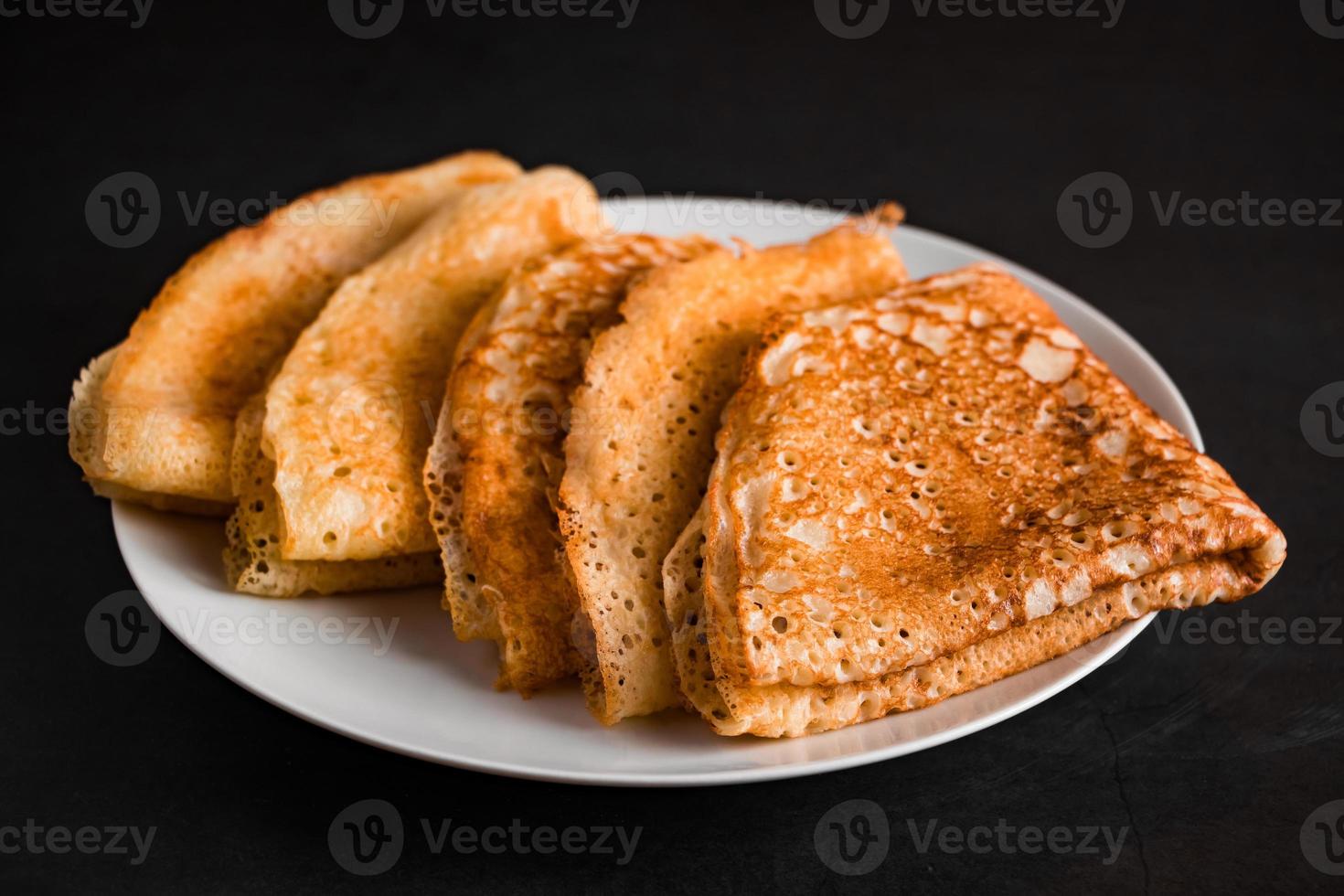 tunna pannkakor på en tallrik på en svart bakgrund, traditionell rysk mat. foto