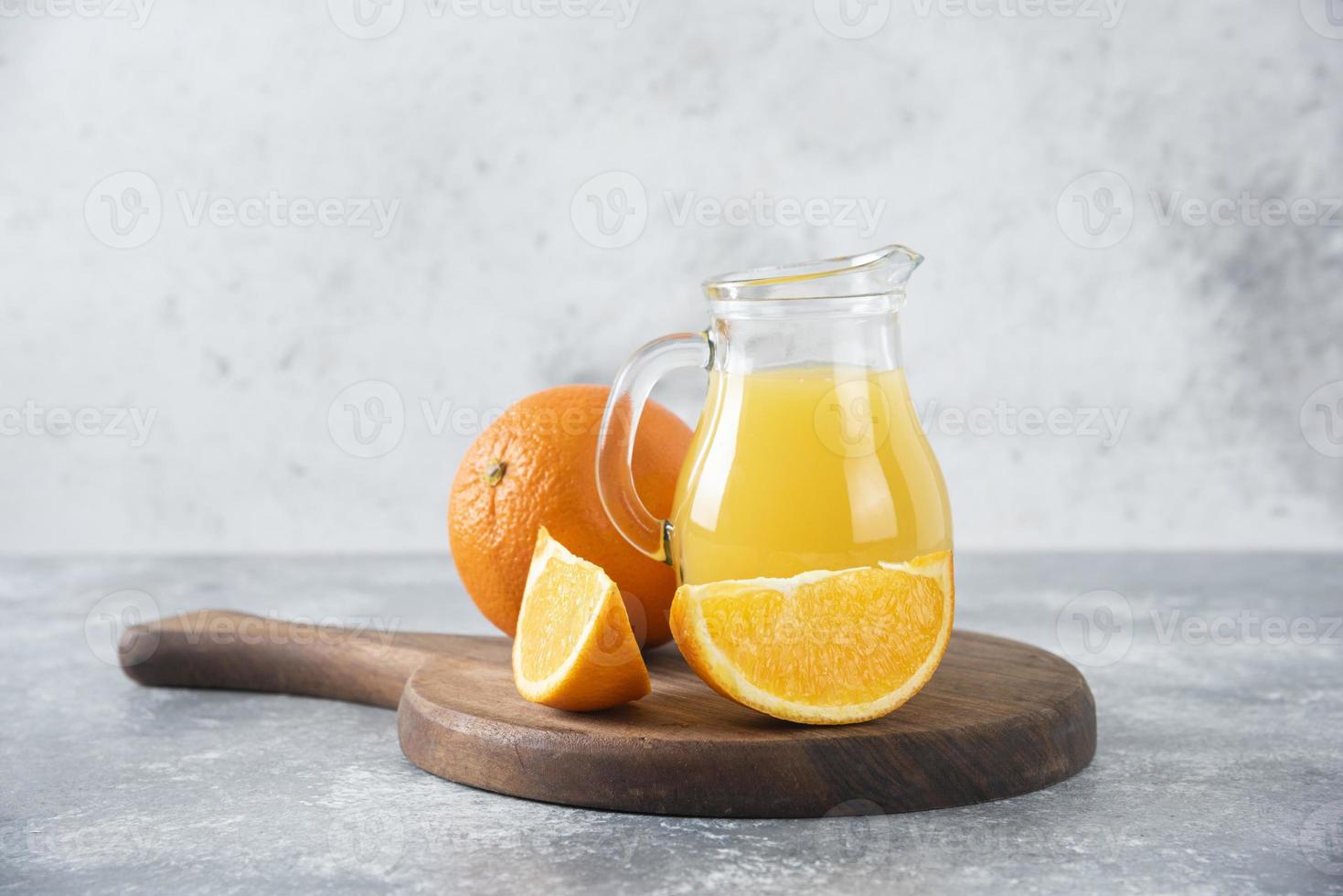en glaskanna med färsk juice med hel och skivad apelsinfrukt placerad på en träskiva foto