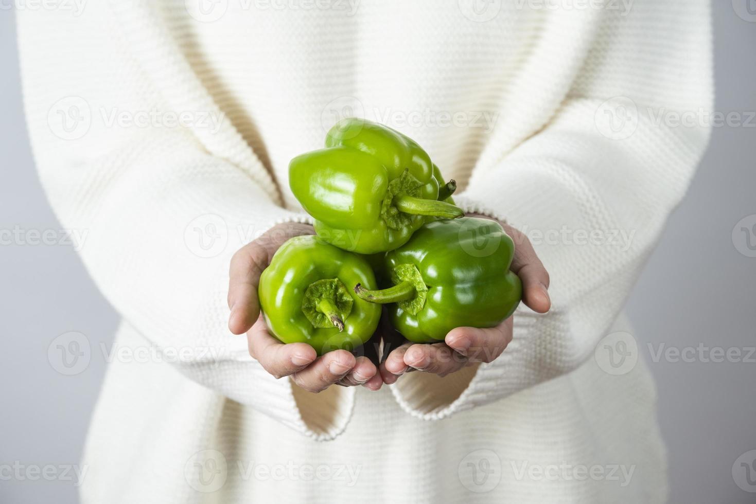 kvinnliga händer som håller en hög med gröna paprika mot en grå vägg foto