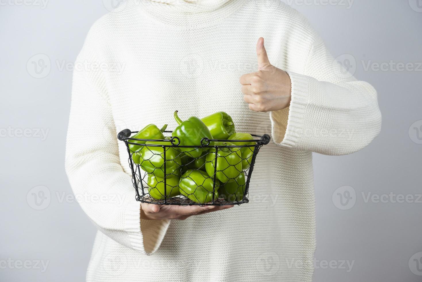 kvinnliga händer med en metallisk korg med gröna paprika som visar tummen foto