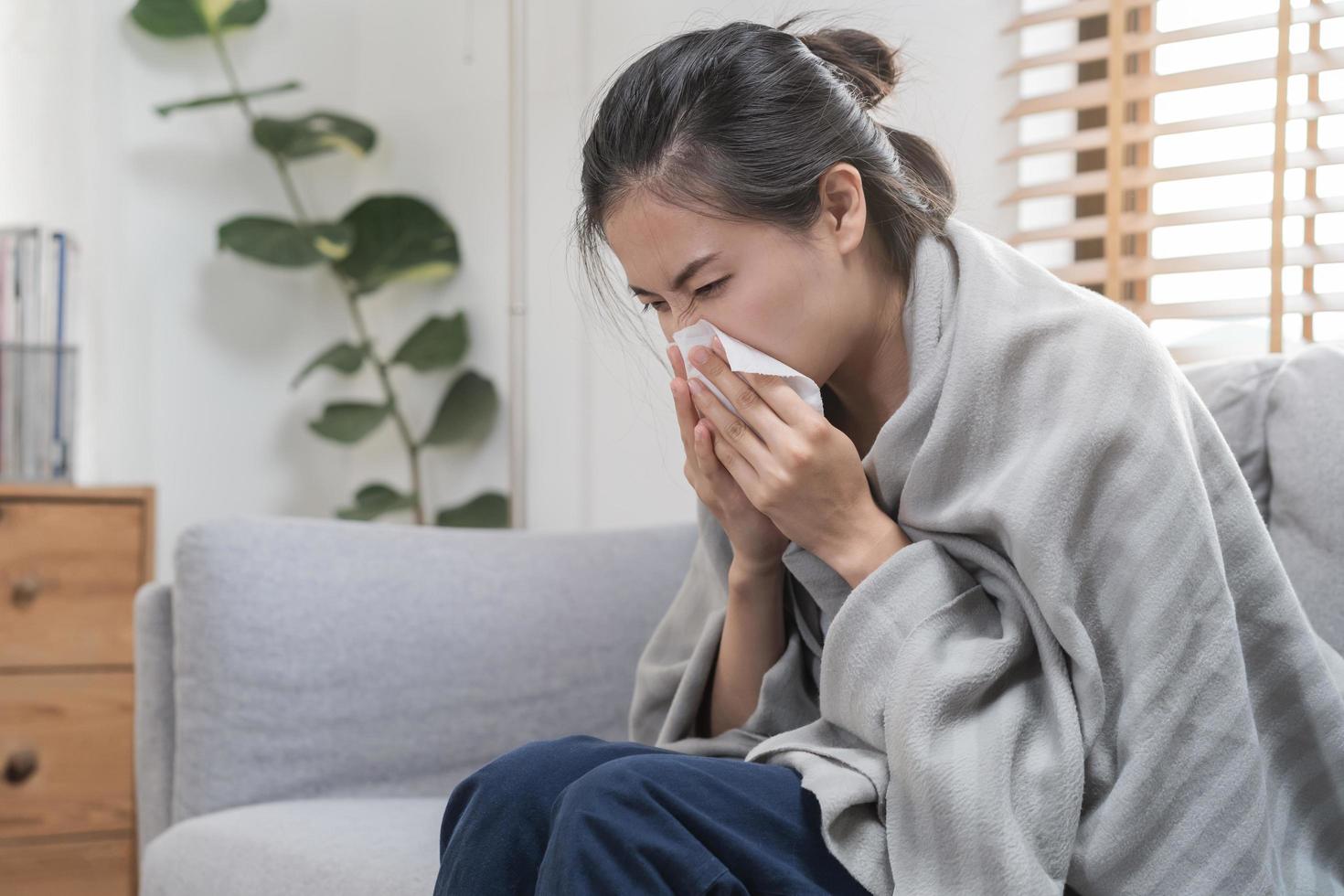 sjuk, coronavirus covid-19 asiatisk ung kvinna, flicka huvudvärk under filt ha en feber, influensa och använda sig av vävnader papper nysning näsa, rinnande Sammanträde på soffa säng på Hem. hälsa vård på virus person. foto