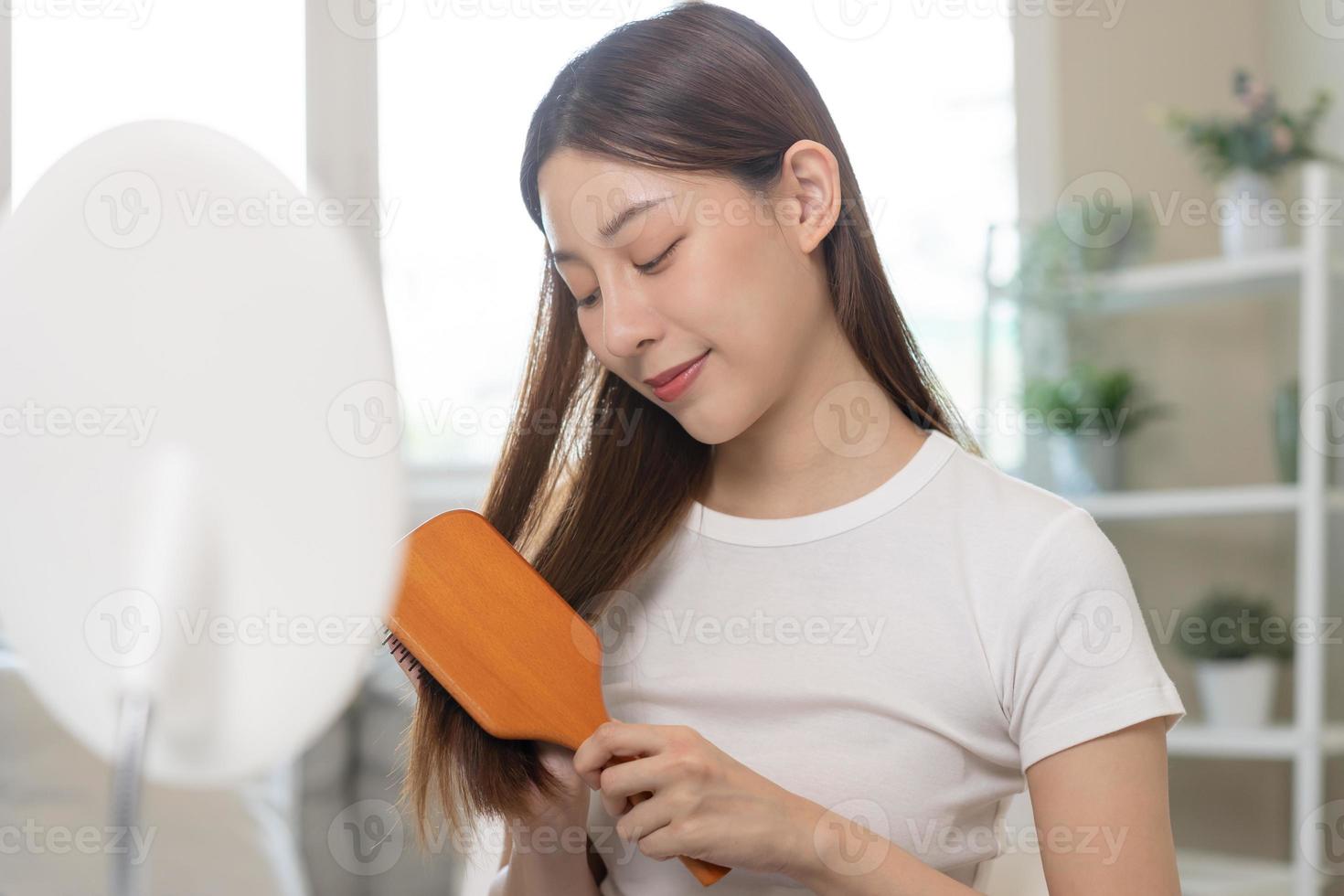 hälsa hår vård, skönhet smink asiatisk kvinna, flicka innehav hårborste och borsta, kammande henne lång hetero hår ser på reflexion i spegel i morgon- rutin- efter salong behandling, frisyr. foto