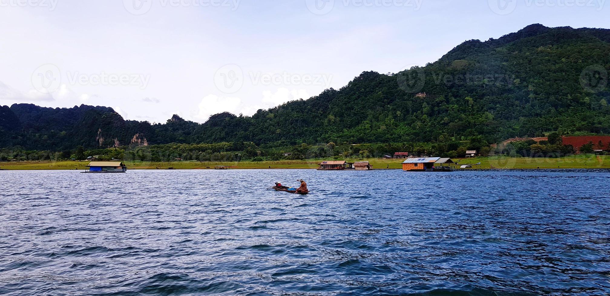 lång svans båt på flod med många Hem eller tillflykt, grön fjäll, blå himmel och moln på srinakarin sjö kanchanaburi, thailand. skön landskap se av naturlig, natur tapet och liv på wate foto