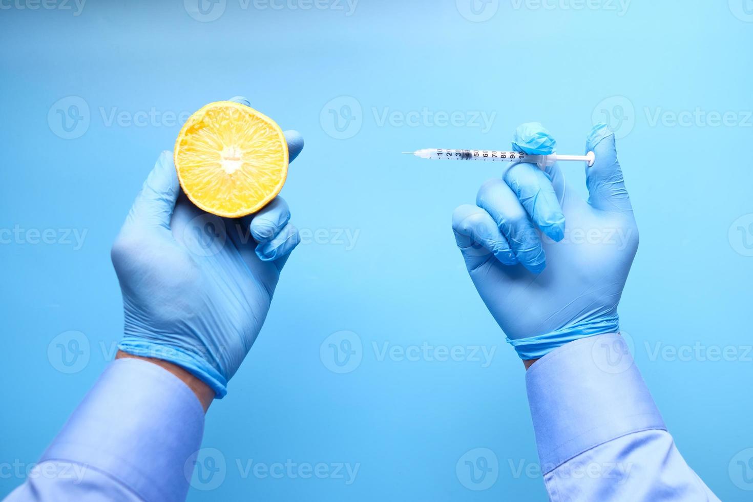 händer i blå handskar som håller citrusfrukter och spruta foto