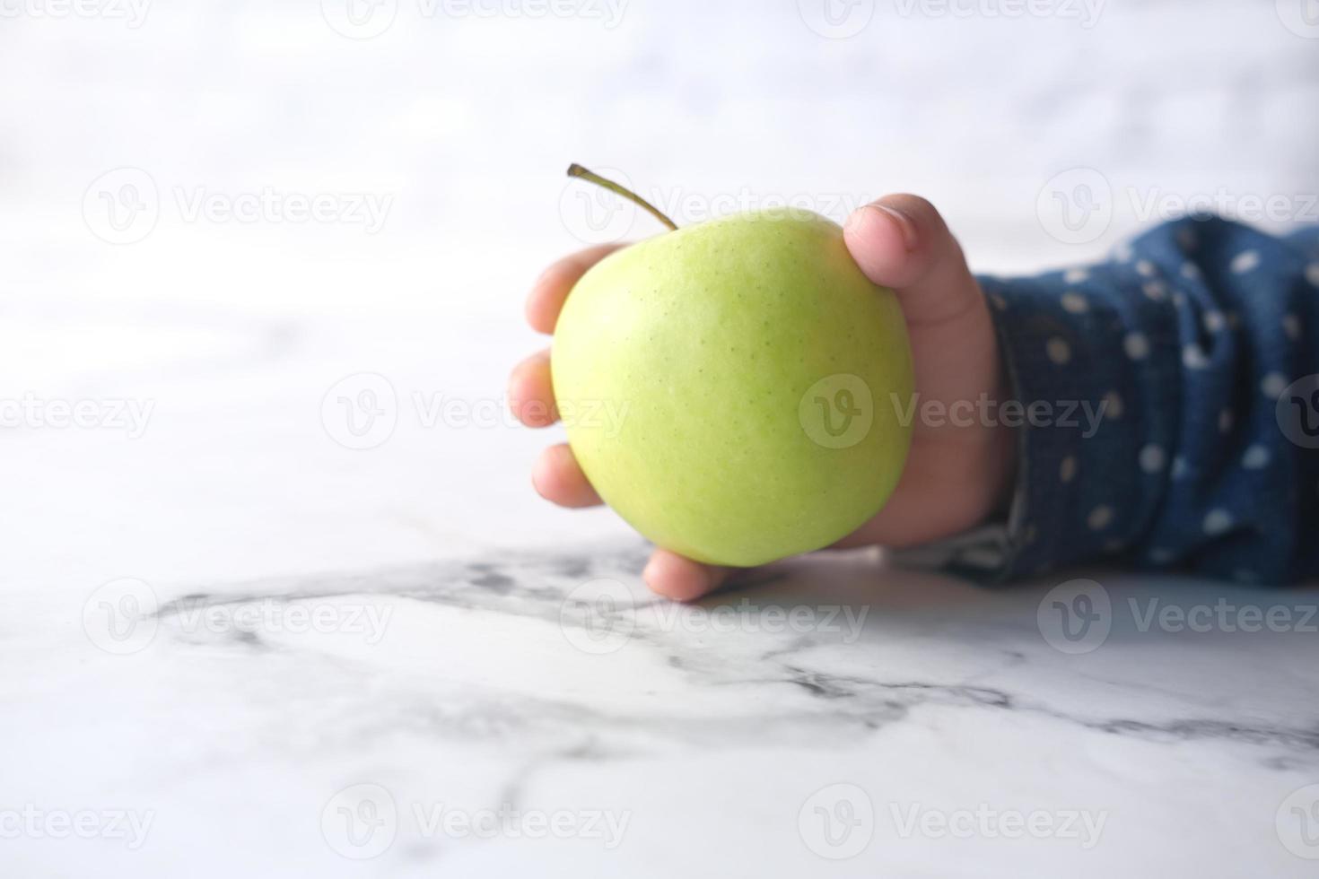 barns hand som håller grönt äpple på neutral bakgrund foto