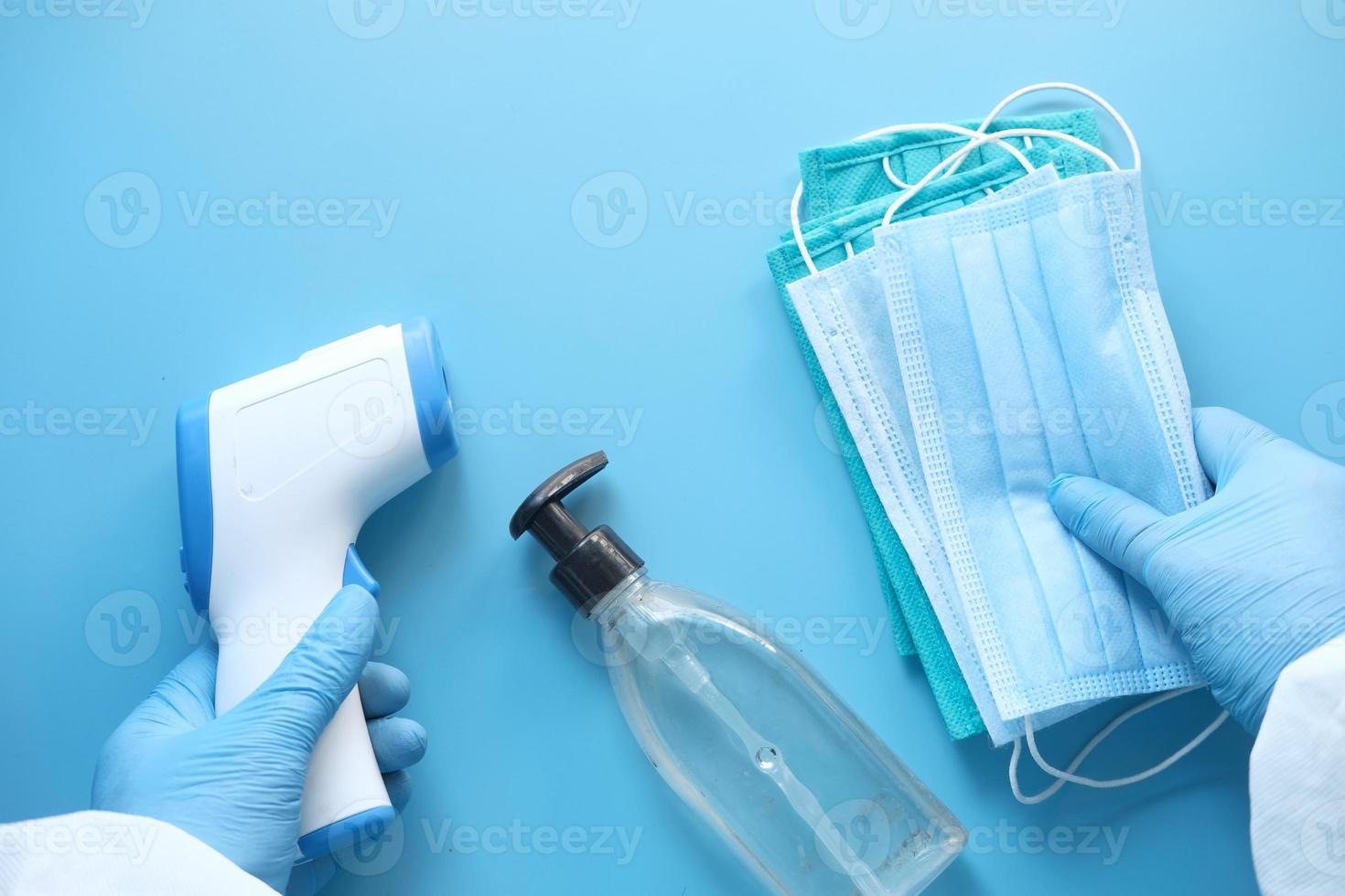 kirurgiska masker, termometer och handdesinfektionsmedel på blå bakgrund foto