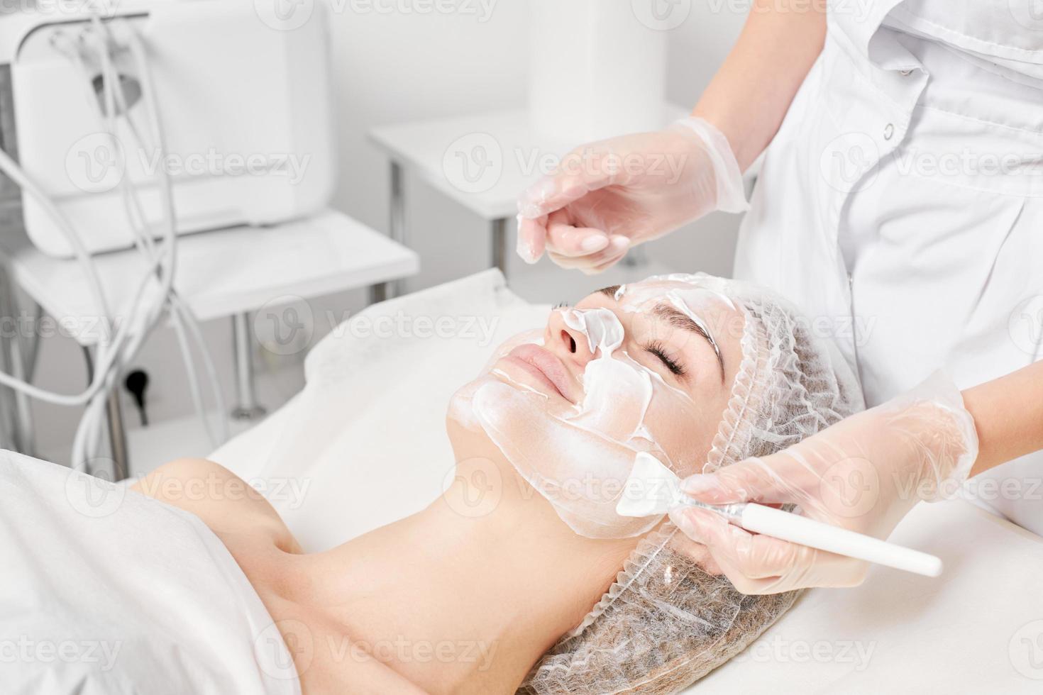 kosmetolog gäller grädde mask på kvinna ansikte för föryngring ansikte hud, procedur i skönhet salong foto