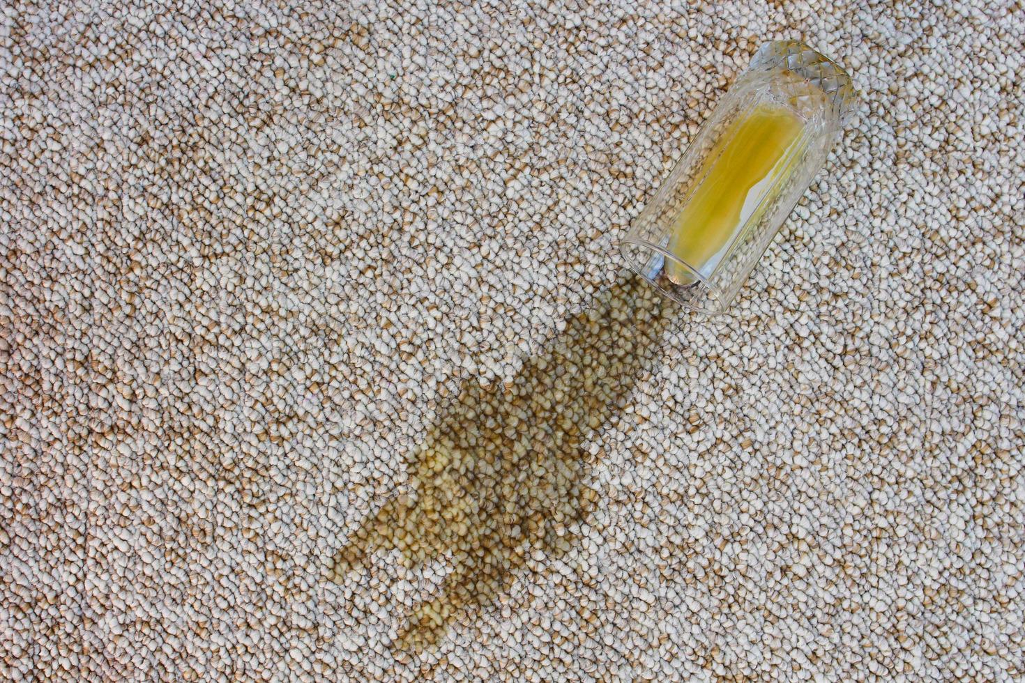 glas av orange juice föll på matta. dryck spillts på golv. svamp och rengöringsmedel. foto