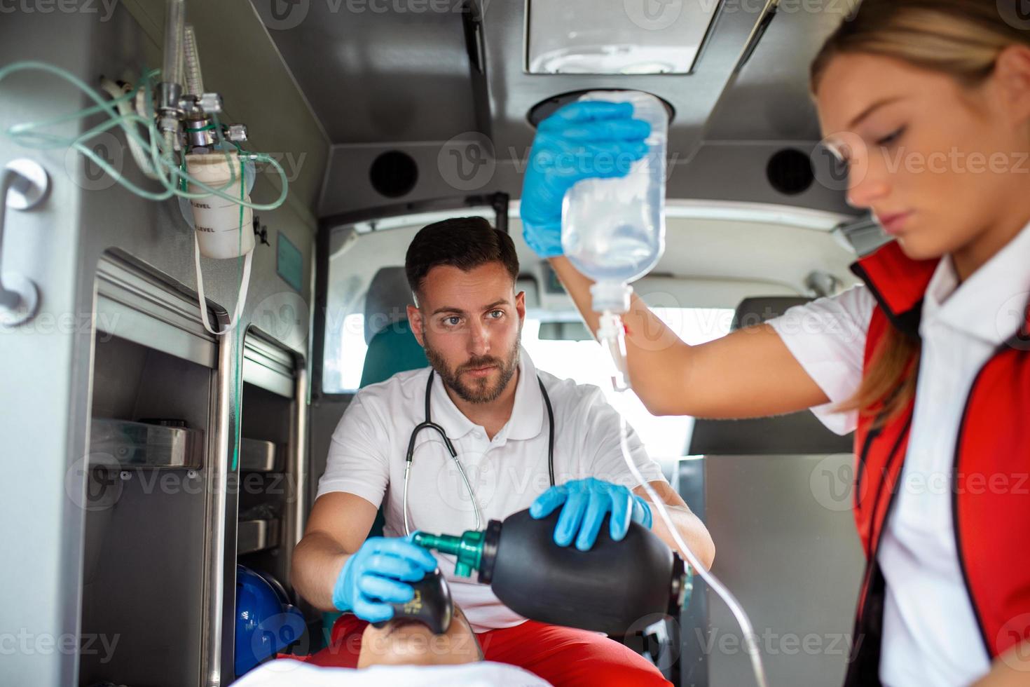 ems paramedics team förse medicinsk hjälp till skadade patient på de sätt till sjukvård sjukhus. nödsituation vård assistent använder sig av en icke-invasiv ventilation mask i ett ambulans. närbild skott. foto