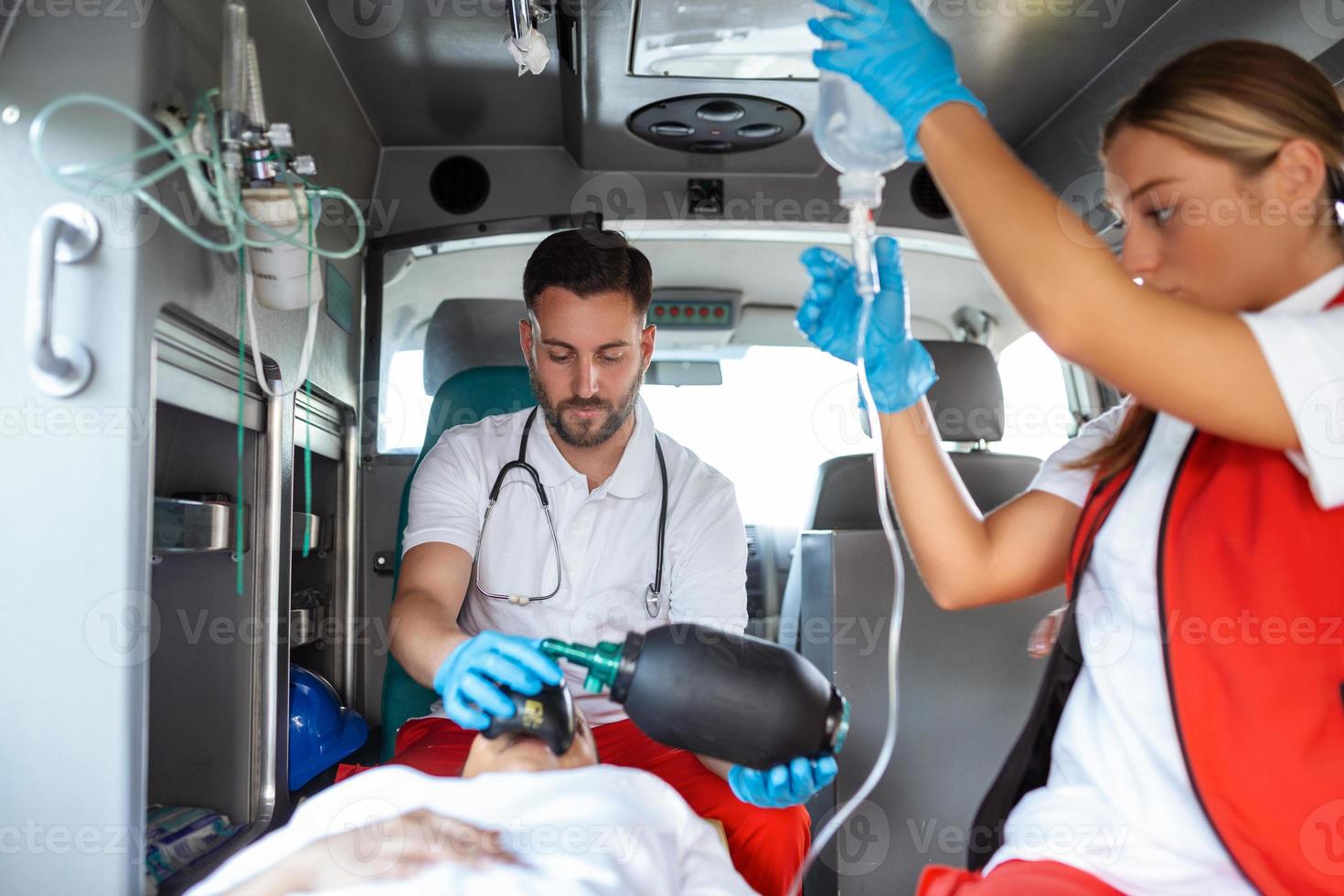se från inuti ambulans av uniformerad nödsituation tjänster arbetare omtänksam för patient på bår under coronavirus pandemisk. foto