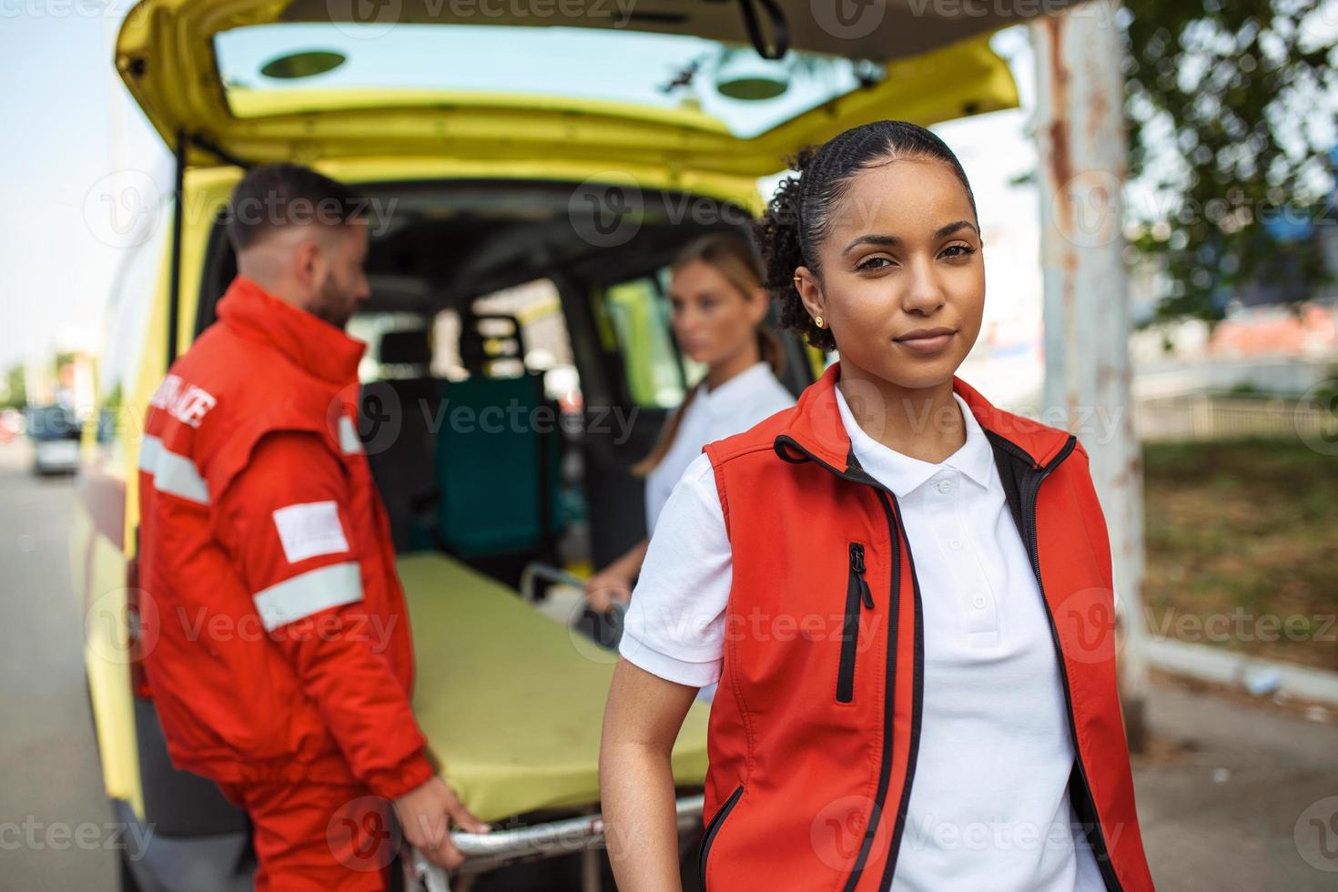 ung kvinna afrikansk amerikan para stående bak- av de ambulans. paramedics förbi de ambulans. två paramedics tar ut strecher från ambulans foto