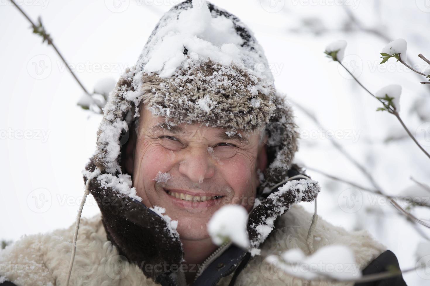 ett äldre man i en vinter- hatt täckt med snö ler och utseende in i de kamera. foto