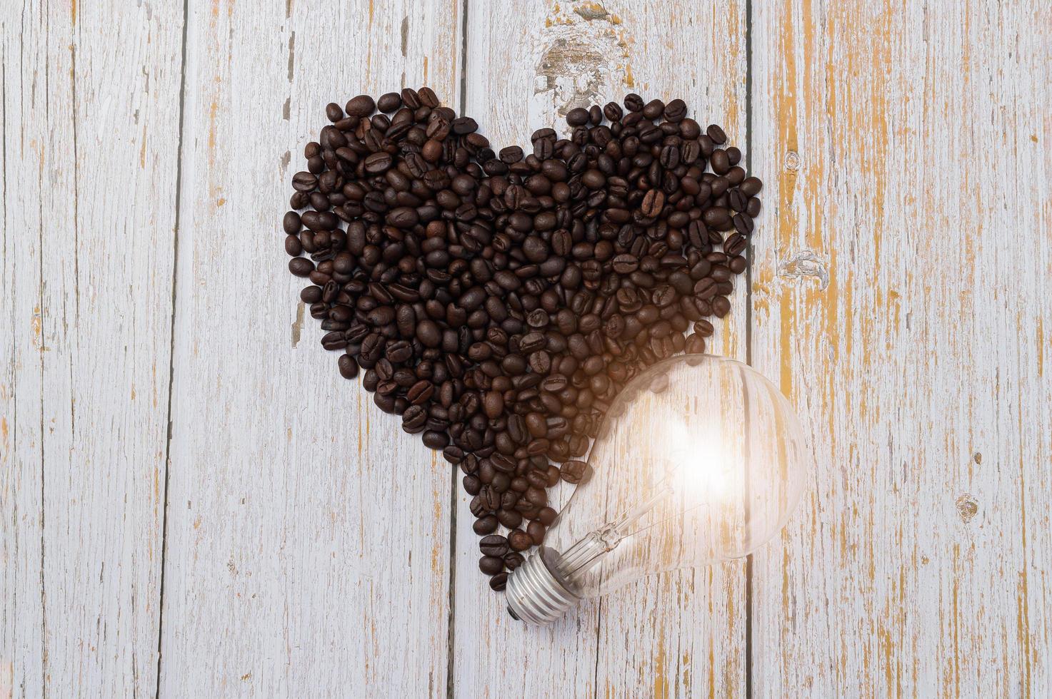 kaffebönor i hjärtform och en glödlampa på ett träbord foto