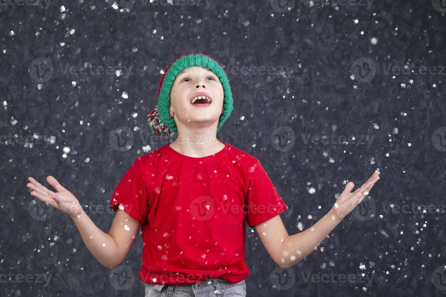 en rolig liten pojke i en röd t-shirt fångster de flygande snö. foto
