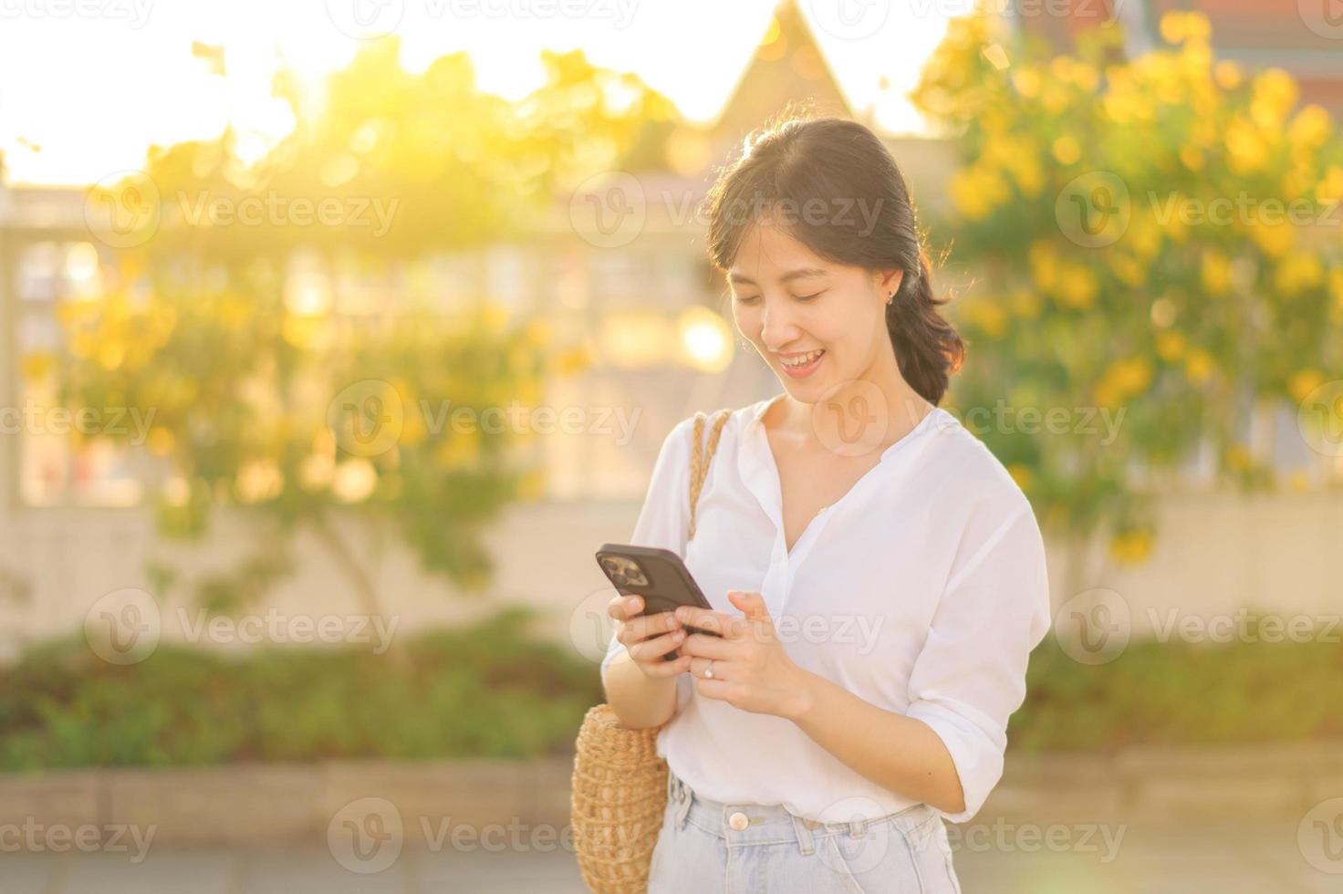 porträtt skön ung asiatisk kvinna med smart mobil telefon runt om utomhus- gata se i en sommar dag foto