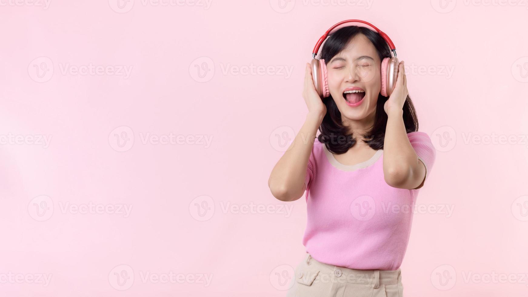 leende Söt modell person lyssna musik låt och njut av dansa med trådlös hörlurar uppkopplad audio radio ljud. positiv roligt exits glad ungdom kvinna kvinna sjunga på rosa isolerat bakgrund studio foto
