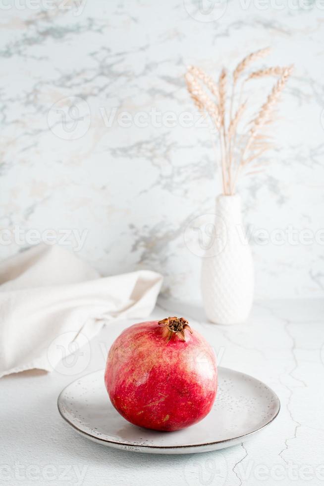 en hela mogen granatäpple på en tallrik på en ljus tabell. organisk naturlig mat. vertikal se foto