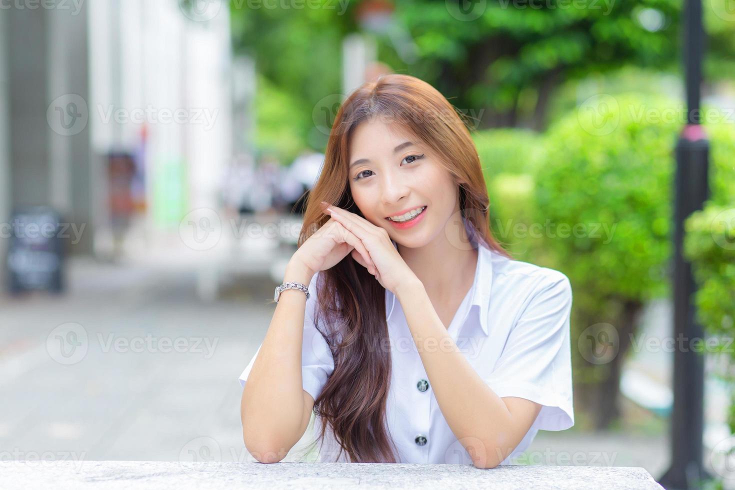 ung thai universitet studerande flicka bär studerande enhetlig medan Sammanträde och leende i de universitet foto