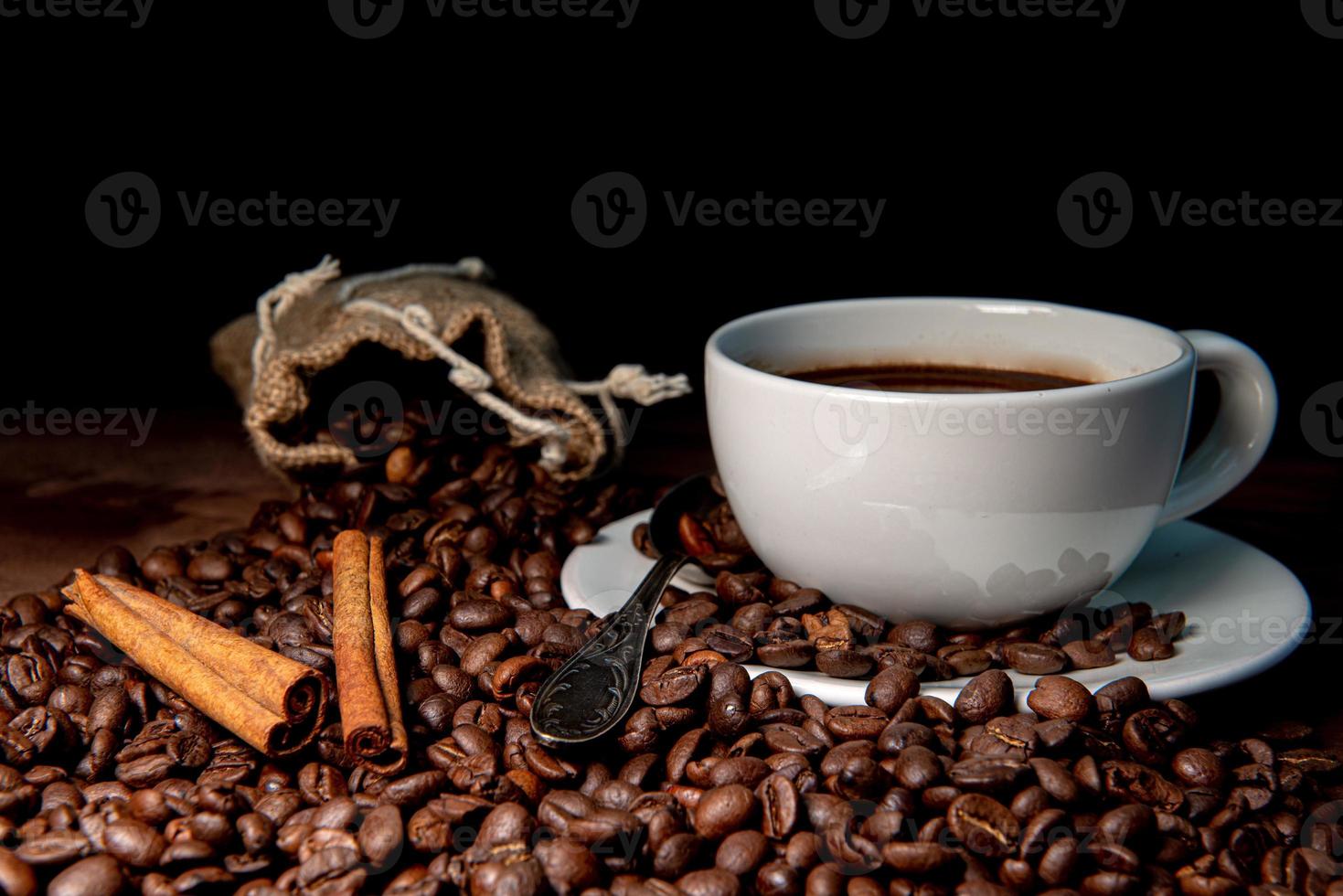 vitt kaffemugg, kanelstänger och kaffebönor på den mörka träbakgrunden foto