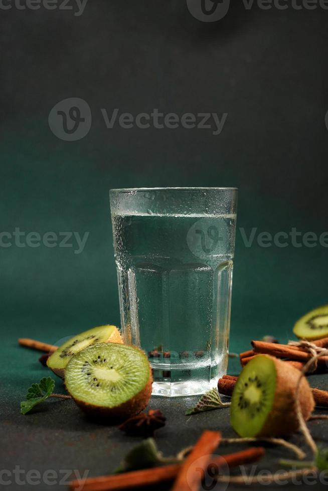 en glas av kall vatten på en grön bakgrund. dekorerad med skiva kiwi, kanel pinnar, badyan, mynta löv. kopia Plats foto