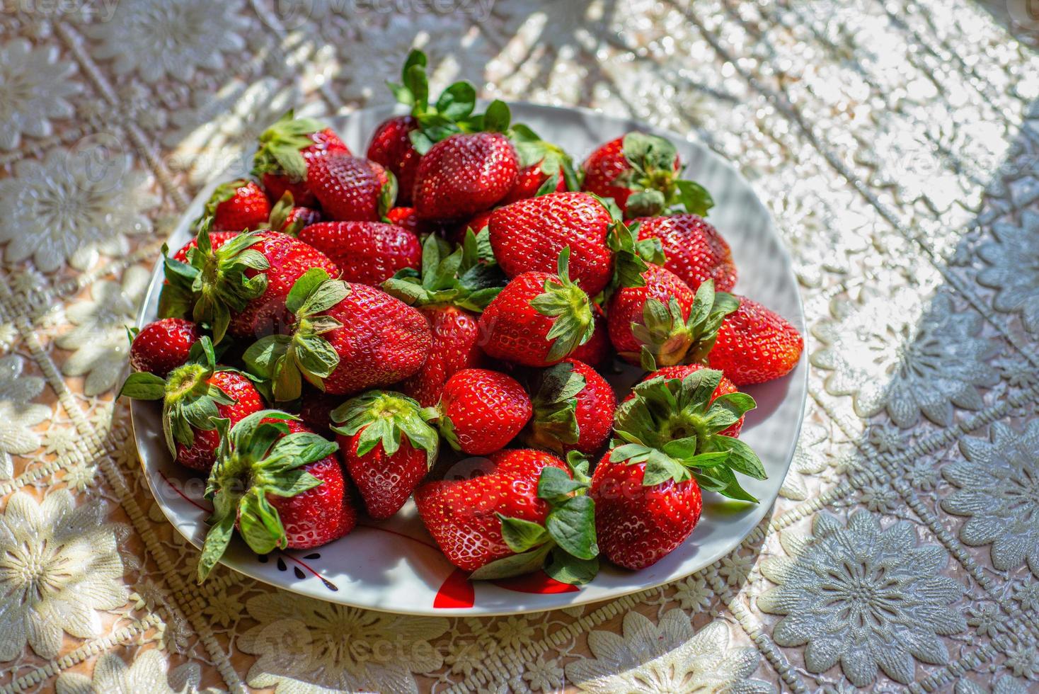 färska jordgubbar på en vit platta, på ett picknickbord foto