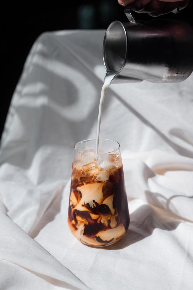 barista hälla mjölk i ett glas iskaffe foto