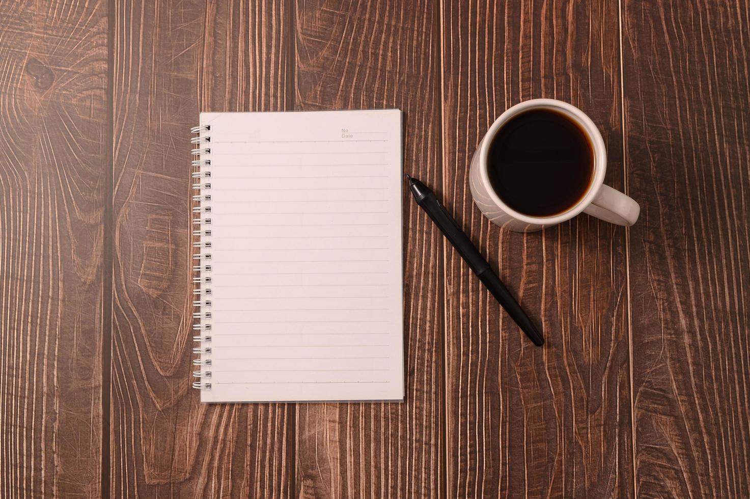 kaffe och en anteckningsbok med en penna på ett träskrivbord foto