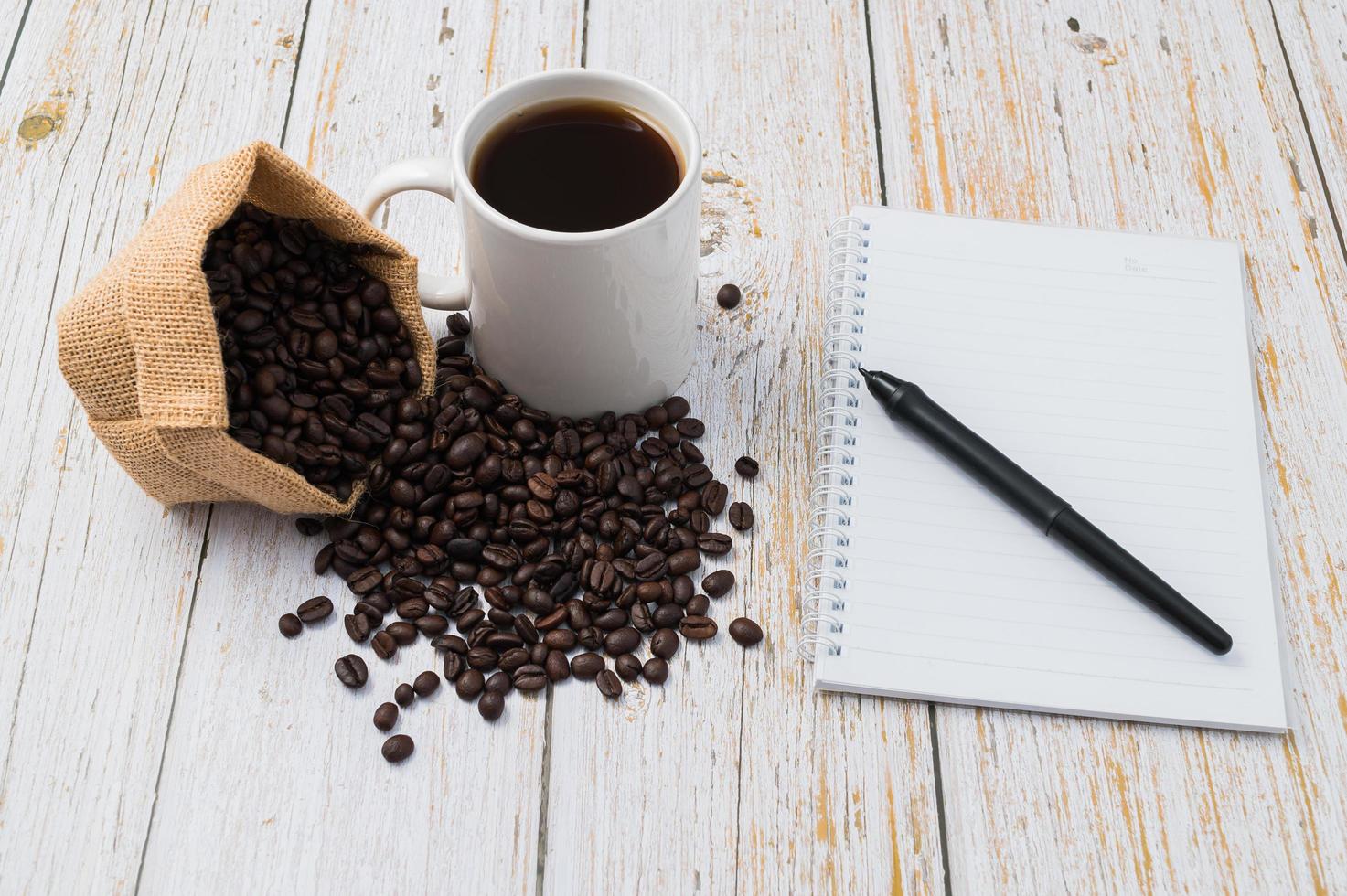 kaffe, kaffebönor och en anteckningsbok med en penna på ett träskrivbord foto