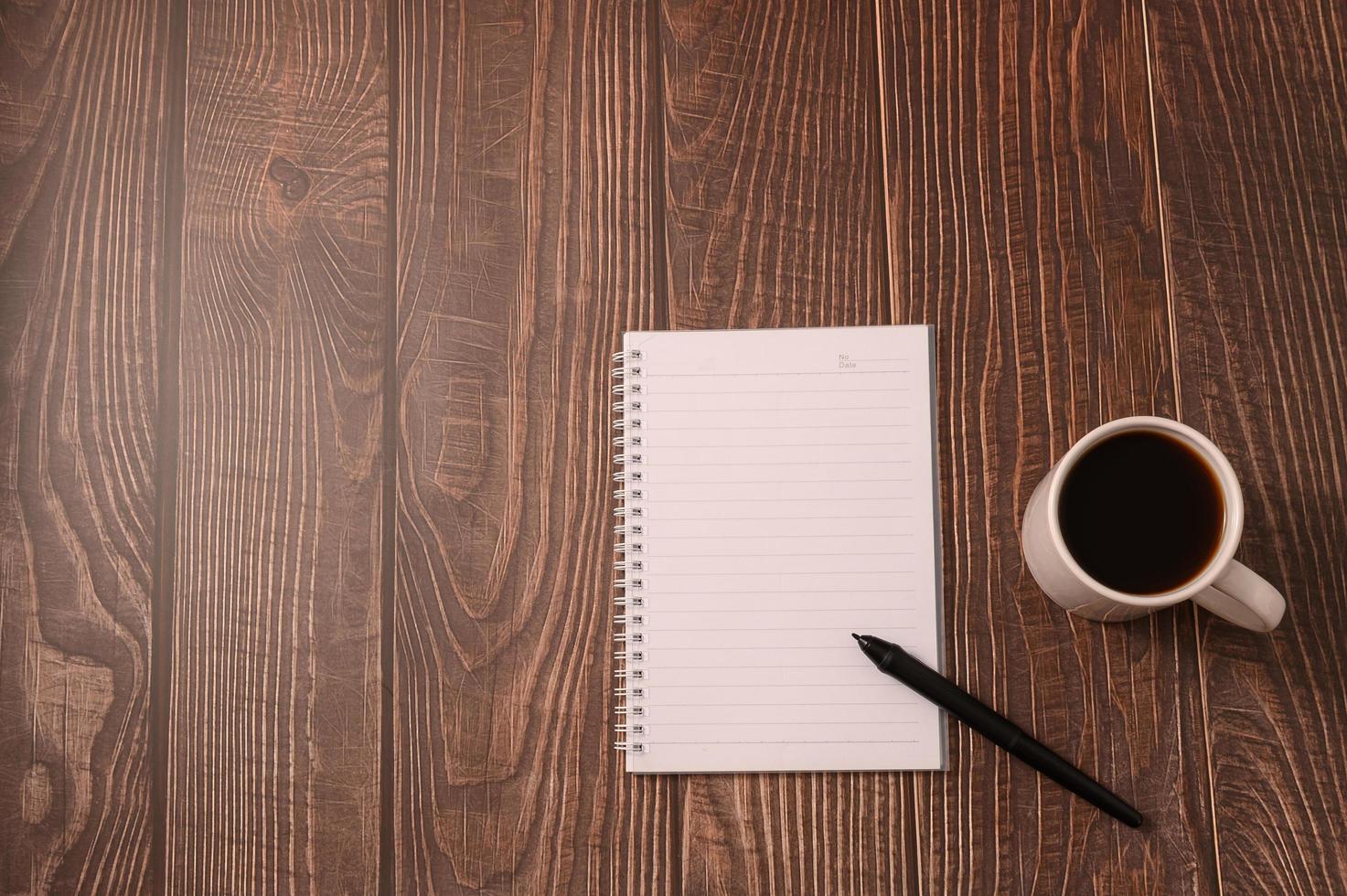 kaffe och en anteckningsbok med en penna på ett träskrivbord foto