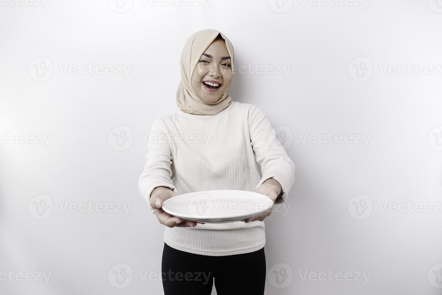 en leende asiatisk muslim kvinna är fasta och hungrig och innehav och pekande till en tallrik foto