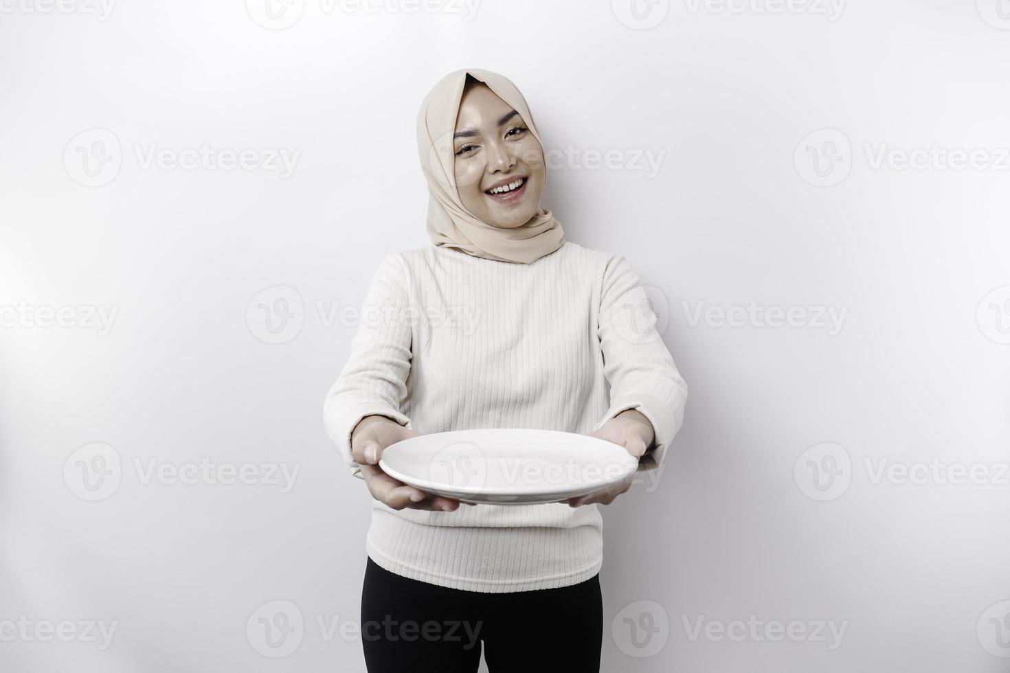 en leende asiatisk muslim kvinna är fasta och hungrig och innehav och pekande till en tallrik foto