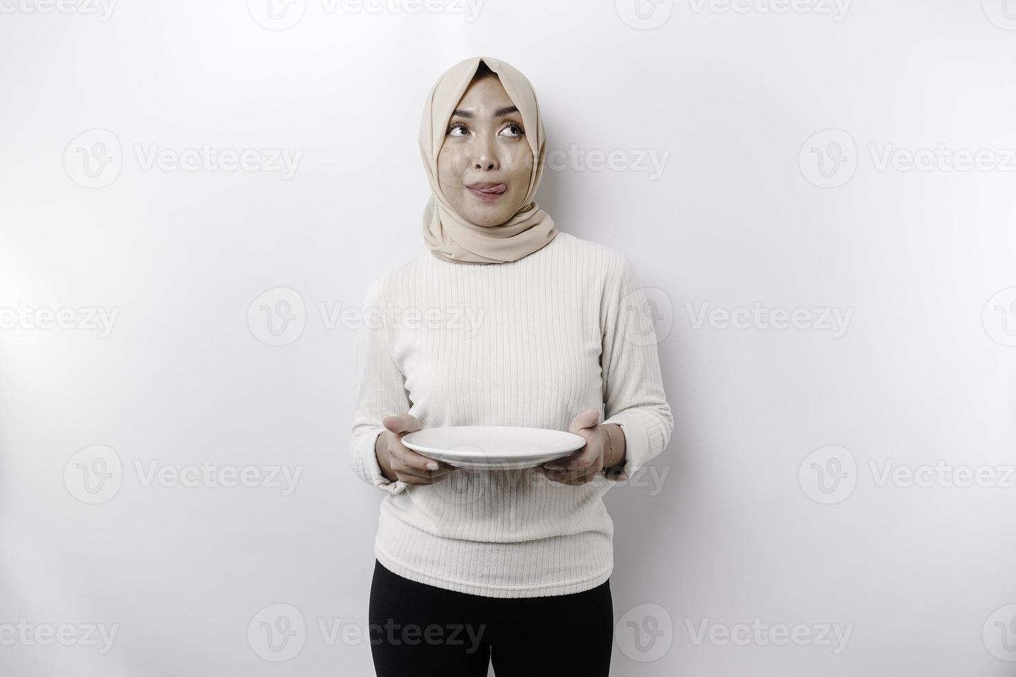 ett asiatisk muslim kvinna är fasta och hungrig och innehav en tallrik medan ser åt sidan tänkande handla om Vad till äta foto