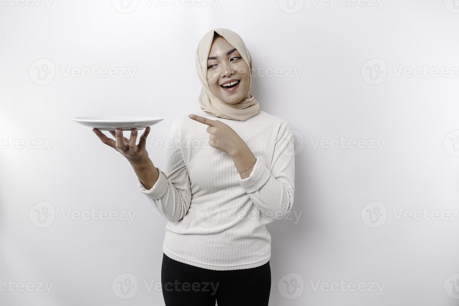 en leende asiatisk muslim kvinna är fasta och hungrig och innehav och pekande till en tallrik foto