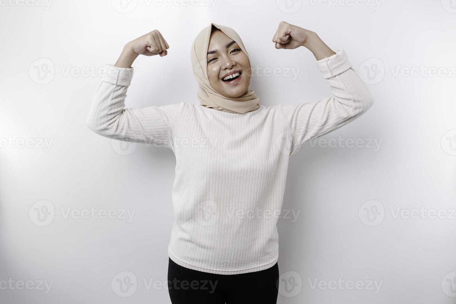 upphetsad asiatisk muslim kvinna bär en slöja som visar stark gest förbi lyft henne vapen och muskler leende stolt foto