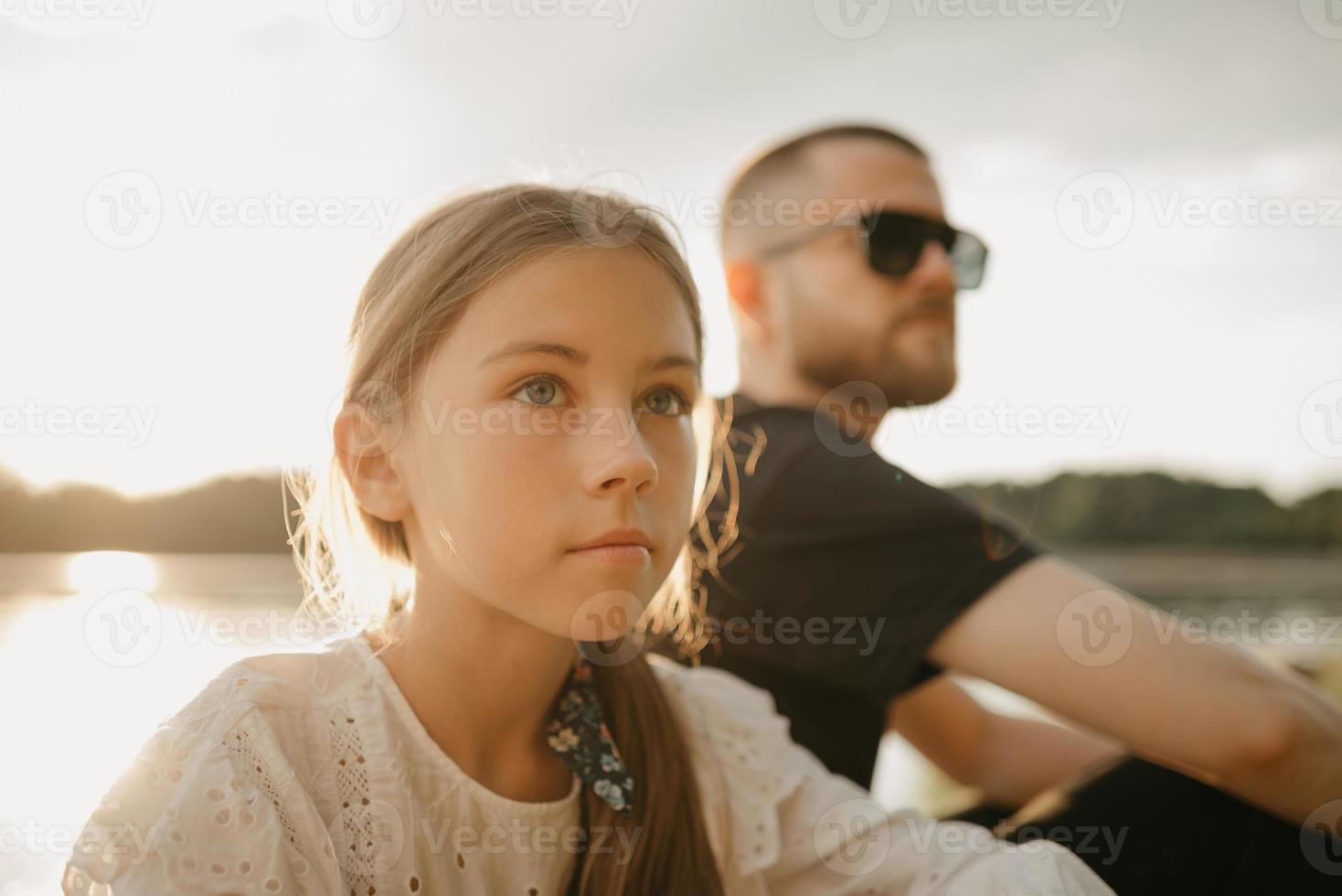 ett nära porträtt av en ung flicka som poserar med sin far med skägg och solglasögon vid kusten foto