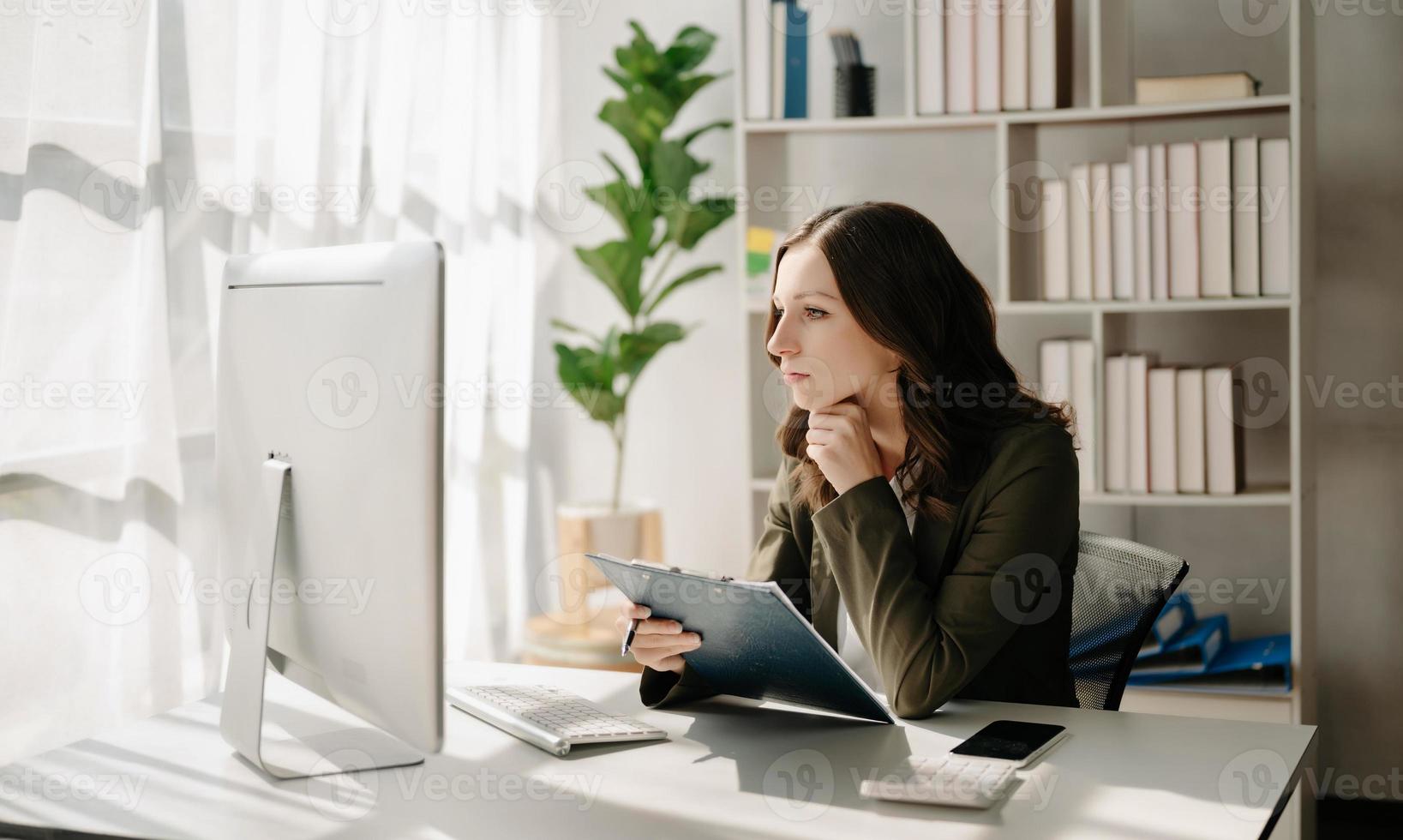 självsäker företag expert- attraktiv leende ung kvinna skriver bärbar dator ang innehav digital läsplatta på skrivbord i kreativ Hem kontor. foto