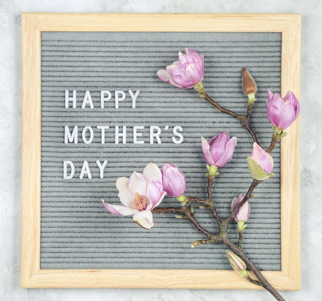 skylt med vita plastbokstäver med citatet glad mors dag och magnoliablommor på grå marmorbakgrund foto