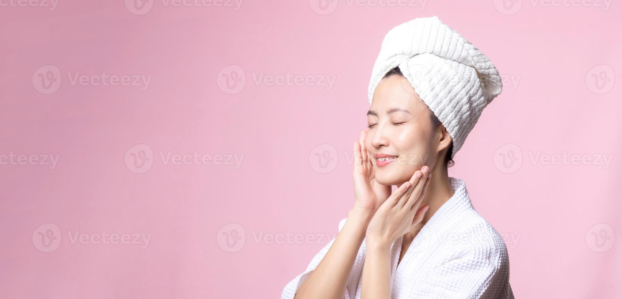 skön ung asiatisk kvinna Lycklig med rena ansikte hud i handduk och morgonrock, spa kostym på rosa bakgrund. hudvård, behandling, wellness terapi, ansiktsbehandling vård, skönhet kvinna hälsa, kosmetologi begrepp foto